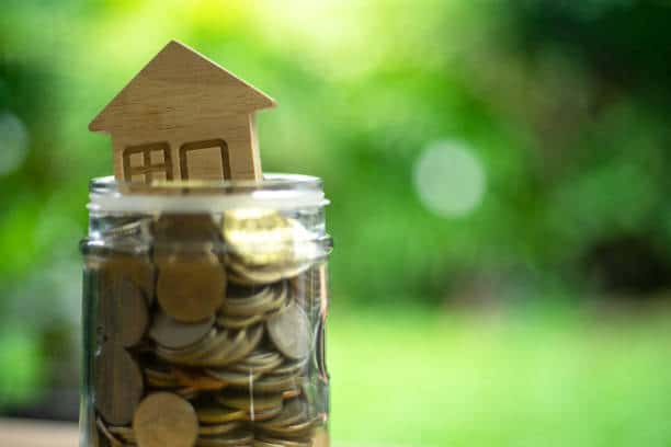 Petite maison en bois dans un bocal plein de pièces de monnaie