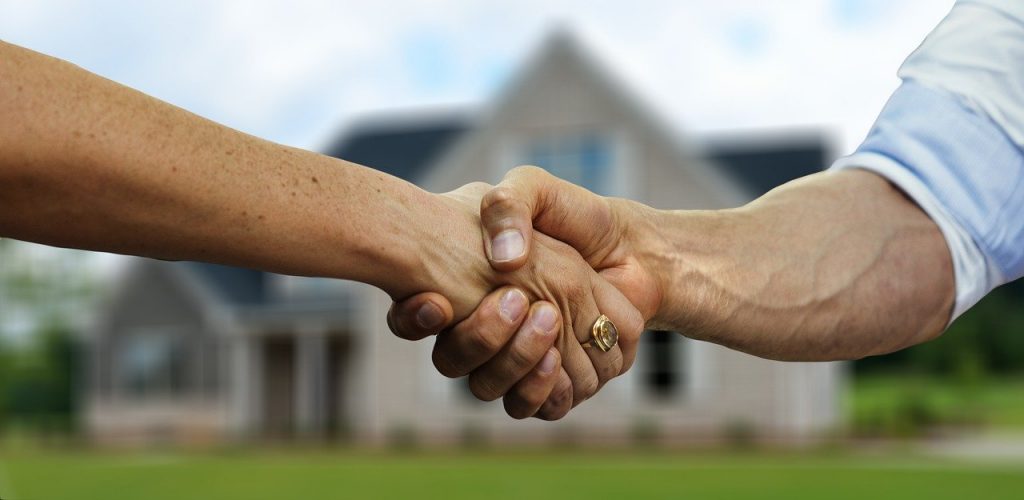 deux personnes qui se serrent la main devant une maison